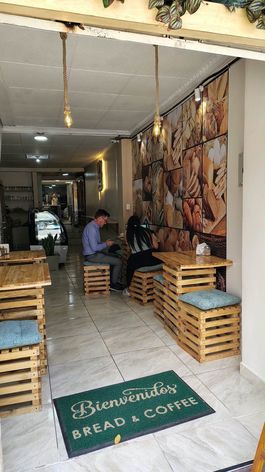 Entrada del local con alfombra de bienvenida y clientes en las mesas