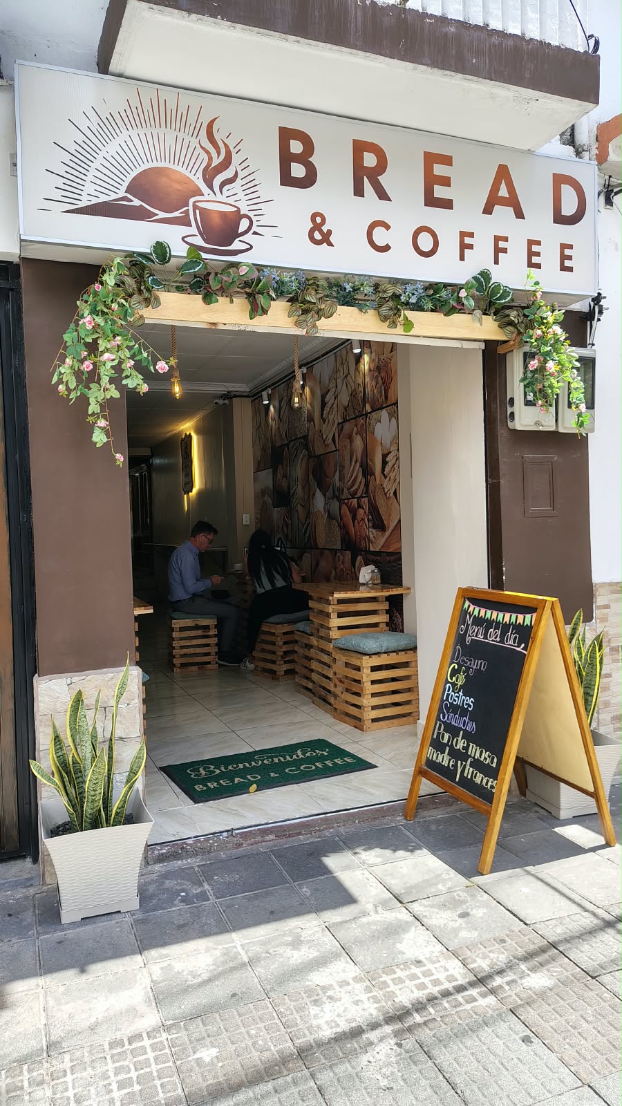 Fachada de Bread & Coffee con letrero, plantas y entrada al local